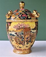 Front view of the Satsuma urn showing detailed oriental scene with multiple human figures and a cart, floral borders, and gold foo dog handles on lid.