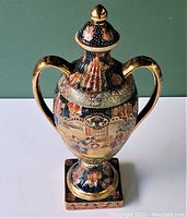 Front view of the ornate Satsuma lidded urn showing detailed painted scene and gold accents on handles and lid.