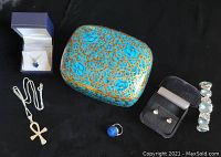 Several sterling silver jewelry pieces and a blue hand-painted lacquered box displayed on black background