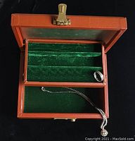 Open orange faux leather jewellery box with green velvet lining showing ring and pendant inside, latch present but key missing, underside of lid lined with faded cloth.