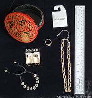 Photo showing red lacquered round box with floral gold and black design, size ruler, Nine West chain necklace on tag, sterling silver ring, Napier earrings in packaging, and black ball bracelet on cord.