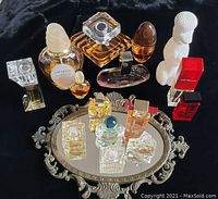 Photo showing the full collection of 15 perfume bottles on the ornate mirror, displaying bottle shapes, colors and arrangement.