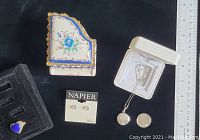 Photo showing porcelain piano-shaped music box with floral decoration, blue and gold accents, Napier earrings in package, open locket with chain, and blue heart-shaped ring on black background with ruler.