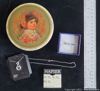 Items displayed on black surface with a measuring ruler showing size references. Ring in blue box, necklace displayed with chain spread out, earrings mounted on Napier card, and marble trinket box with colorful lid featuring Edna Hibel print.