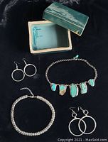 Photo showing handmade green clay trinket box with lid open, two necklaces and two sets of hoop earrings laid out on black background.
