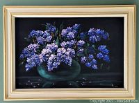 Front view of the framed floral oil painting on black velvet featuring blue and white flowers in a green vase, signed 'Vicki'.