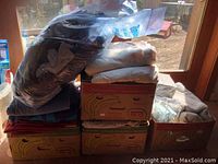 Two Rubbermaid bins stacked with multiple folded clothing items including sweaters and pants, some plastic bags visible on top.