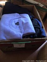 Box with folded men's sweaters, light purple and blue visible