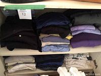 Interior of white cabinet showing two shelves of folded men's clothing including dark and light colors, primarily shirts and sweaters.