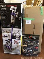 Three boxes: Dyson Cyclone V10 Animal vacuum package, cardboard box containing vacuum stand, and VaccuFlex hose packaging