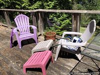 Two Adirondack chairs, one purple and one beige, with matching plastic footrests and a purple folding side table on a wooden deck.