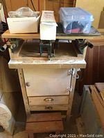 Full view of the workbench showing the wooden construction, cabinet door at the front, and two storage drawers above the base platform.