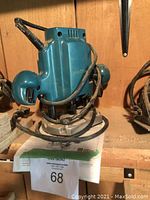 Front view of teal Makita plunge router sitting on wooden shelf