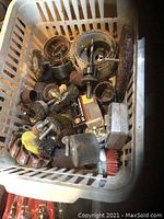 Photo showing assorted grinder and sanding attachments including wire brushes, sanding drums, polishing pads, and other tool accessories inside a white plastic basket.