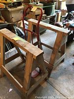 Two wooden saw horses standing side by side in a cluttered garage showing wear and age.