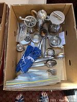 Top-down view of assorted silver items in a cardboard box showing various serving pieces and utensils.