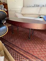 Side angle of the oval-shaped solid wood coffee table showing wood grain and metal legs.