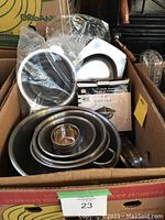 Box containing a set of stacked stainless steel mixing bowls of various sizes along with some small cups inside the largest bowl.