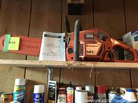 Full view of chainsaw on shelf with bar cover and manual