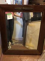 Front view of the wooden framed mirror showing decorative carved leaf detail at the top center of the frame and clear mirror surface reflecting surrounding room.