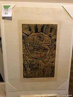 Photo of framed artwork with abstract design in dark tones on light paper, secured by corner protectors.