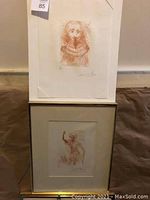 Both prints displayed stacked against wall, male unframed above framed female