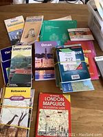 Photo capturing assortment of travel maps including Indian Subcontinent, Amsterdam, Saint Lucia, Oman, Botswana, London MapGuide and more spread on a table.