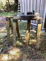 Photo showing a pair of wooden sawhorses supporting a black plastic item which is a tree watering ring.