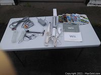 Nintendo Wii console setup with controller, nunchuck, fishing rod accessory, power and AV cables, manuals, and multiple game discs arranged on white table.