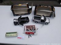 Overview of Swiss Army multi-tool, Victorinox box, and two cast metal model cars (Ford F-150 and Boss Mustang) on a white surface.