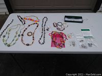Photo showing assorted costume jewelry on white table, including necklaces, bracelets, earrings and pins