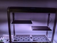 Black metal frame with two adjustable shelves and two gray pod trays