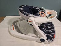 Side view of Fisher-Price Sit-Me-Up Floor Seat showing navy floral patterned seat and white plastic frame.