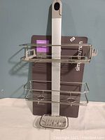 Simplehuman adjustable shower caddy in packaging with two wire shelves and soap dish shown flat against a wall