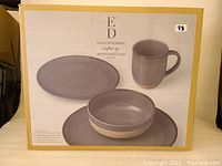 Photo of unopened box showing graphic of grey 16-piece dinnerware set with plates, bowls, and mugs.