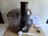 Full view of Hamilton Beach Big Mouth juice extractor with missing pitcher, displayed on cardboard with cleaning brush and manual behind.