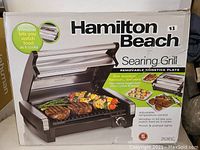 Photo of Hamilton Beach searing grill box showing the product by itself with text highlighting removable nonstick plate and viewing window feature.