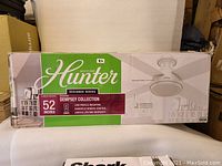 Box front showing Hunter Dempsey 52-inch ceiling fan branding and product features: large room, indoor use, handheld remote, limited lifetime warranty.