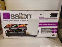 Box of Salton party grill showing brand and model with packaging damage.