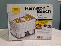 Photo of the original packaging showing front view of the Hamilton Beach food dehydrator and its key features.