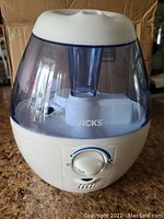 Full view of the humidifier showing translucent blue water tank and white base with Vicks logo.