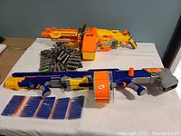 Two Nerf blasters and foam dart magazines with loose foam darts spread on a white surface
