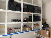 Multiple small black plastic toolboxes and various items on shelving units