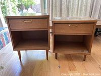 Pair of wooden end tables shown side by side, one with shorter legs, placed on wooden floor indoors.