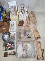 Overview photo showing six wood carved figurines including seated and standing figures, a carved elephant, fish, and parrot, decorative votives, and shell items spread on carpet.