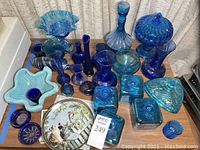 Full lot view showing blue glass candy dishes with lids, multiple blue glass vases, pedestal dishes, ceramic starfish bowl, and decorative plates.