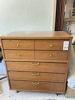 Front view of wood dresser showing five drawers with brass tone pulls and laminate top.