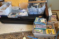 Overview of large tub and smaller boxes on couch with assorted crafting books, magazines, and containers