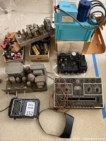 Overview shot showing two tube amplifier chassis, vacuum tube tester front panel, portable radio, shoeboxes of tubes, and Little Giant condensate pump