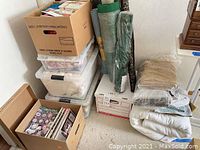 Six boxes containing fabric, craft magazines, and embroidery supplies stacked in a corner